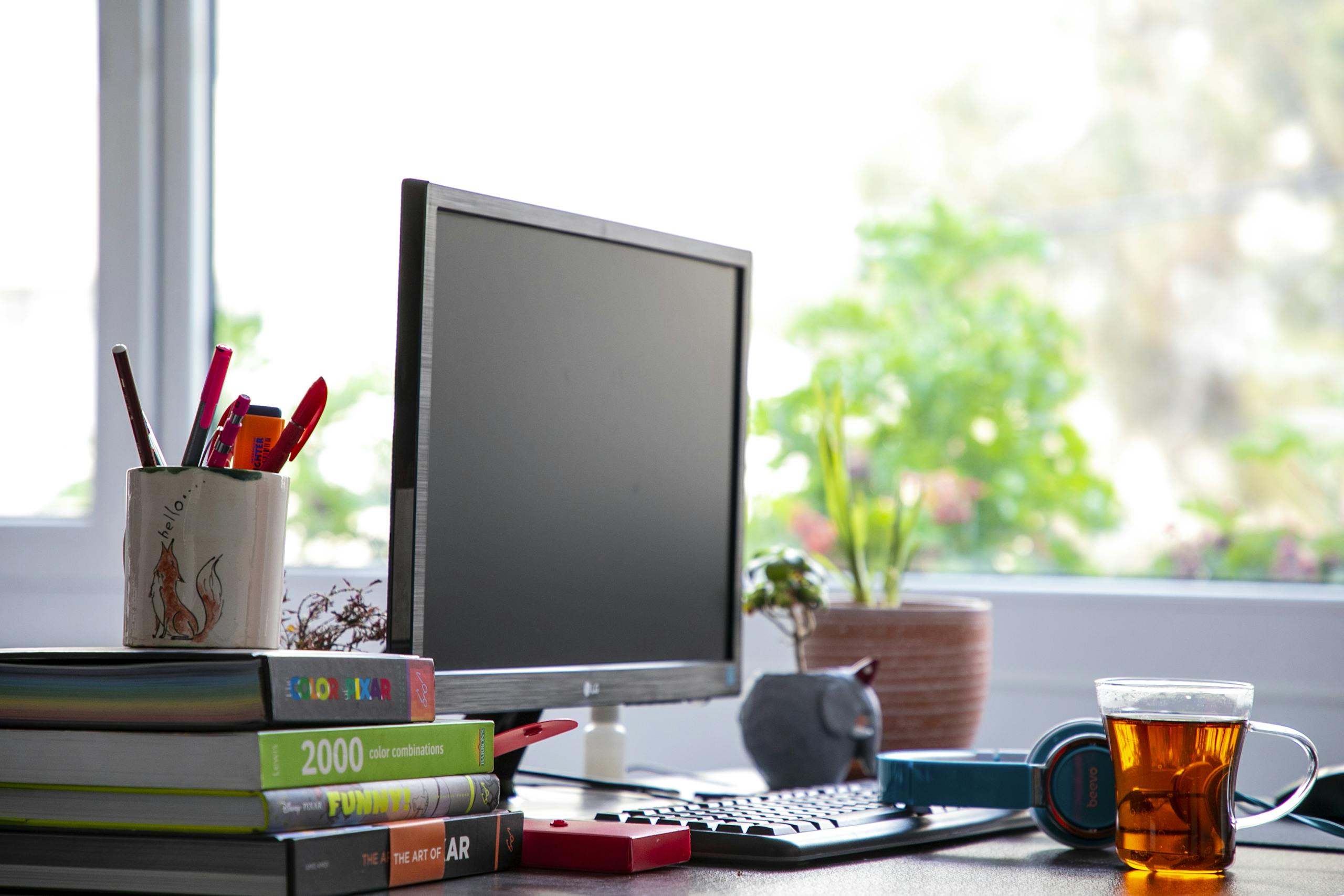 Modern office desk setup with a computer, books, and a cup of tea for a creative work environment.